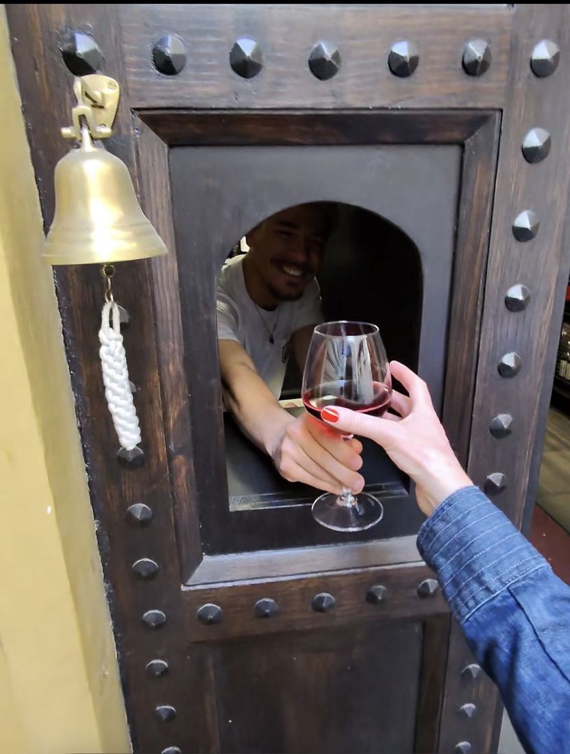 A hand reaching through a wine window to take a glass of red